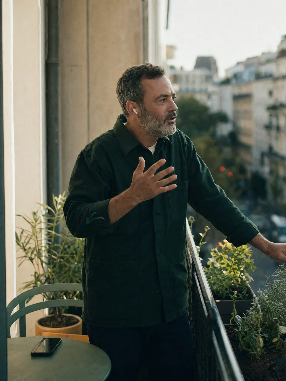 A candidate on his balcony at dusk, earbuds in, explaining something with his hands mid-conversation